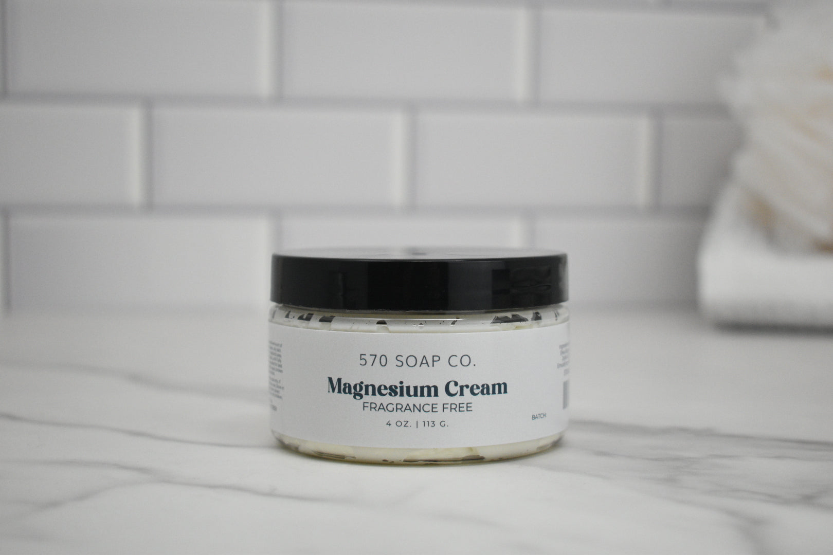 Jar of 570 Soap Co. Magnesium Cream on a marble surface with tiled wall background