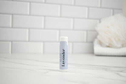 Lip balm labeled 'Lavender' on a bathroom counter with a tiled wall background