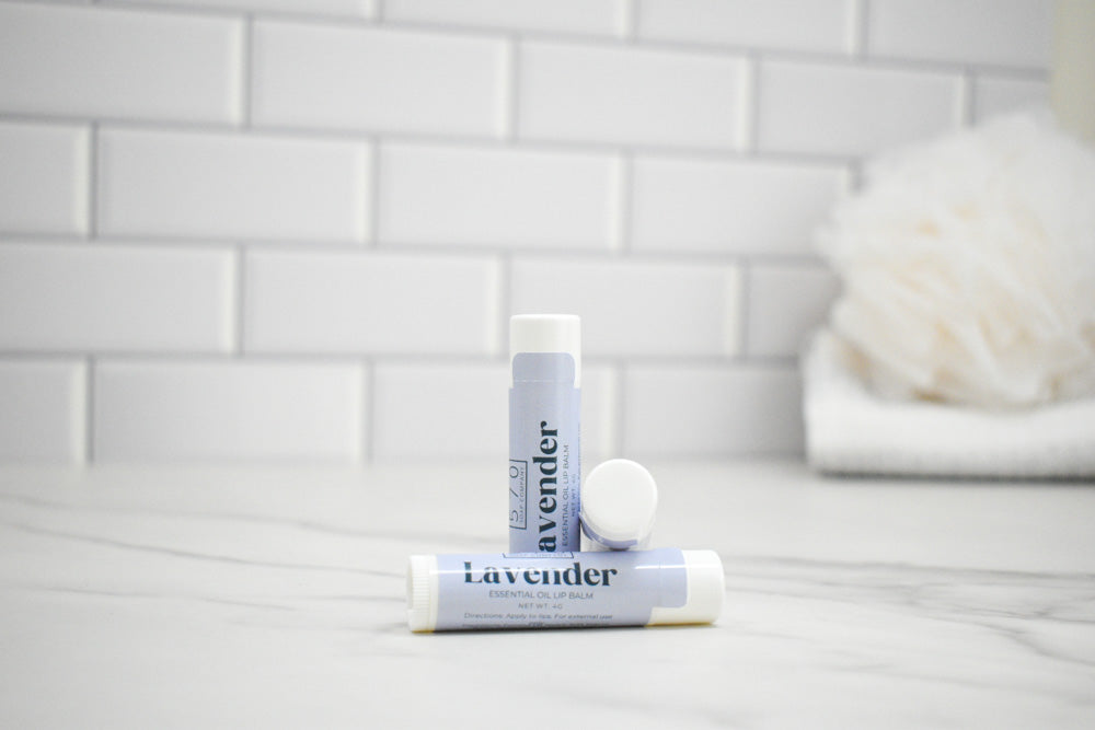 Two lavender-scented lip balms on a bathroom counter with a tiled wall background.