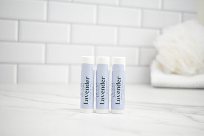 Three lavender-scented products on a white surface with a tiled wall background