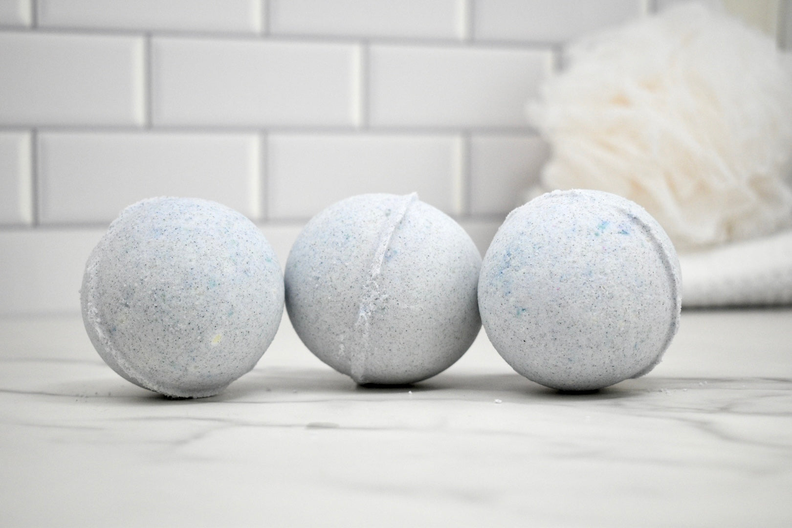 Three bath bombs on a marble surface with a tiled wall background