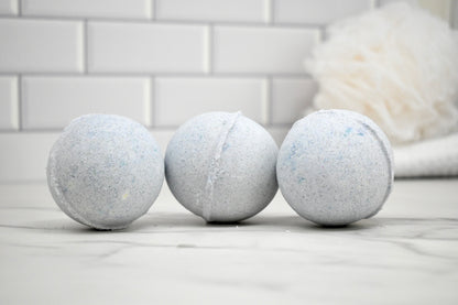 Three bath bombs on a marble surface with a tiled wall background