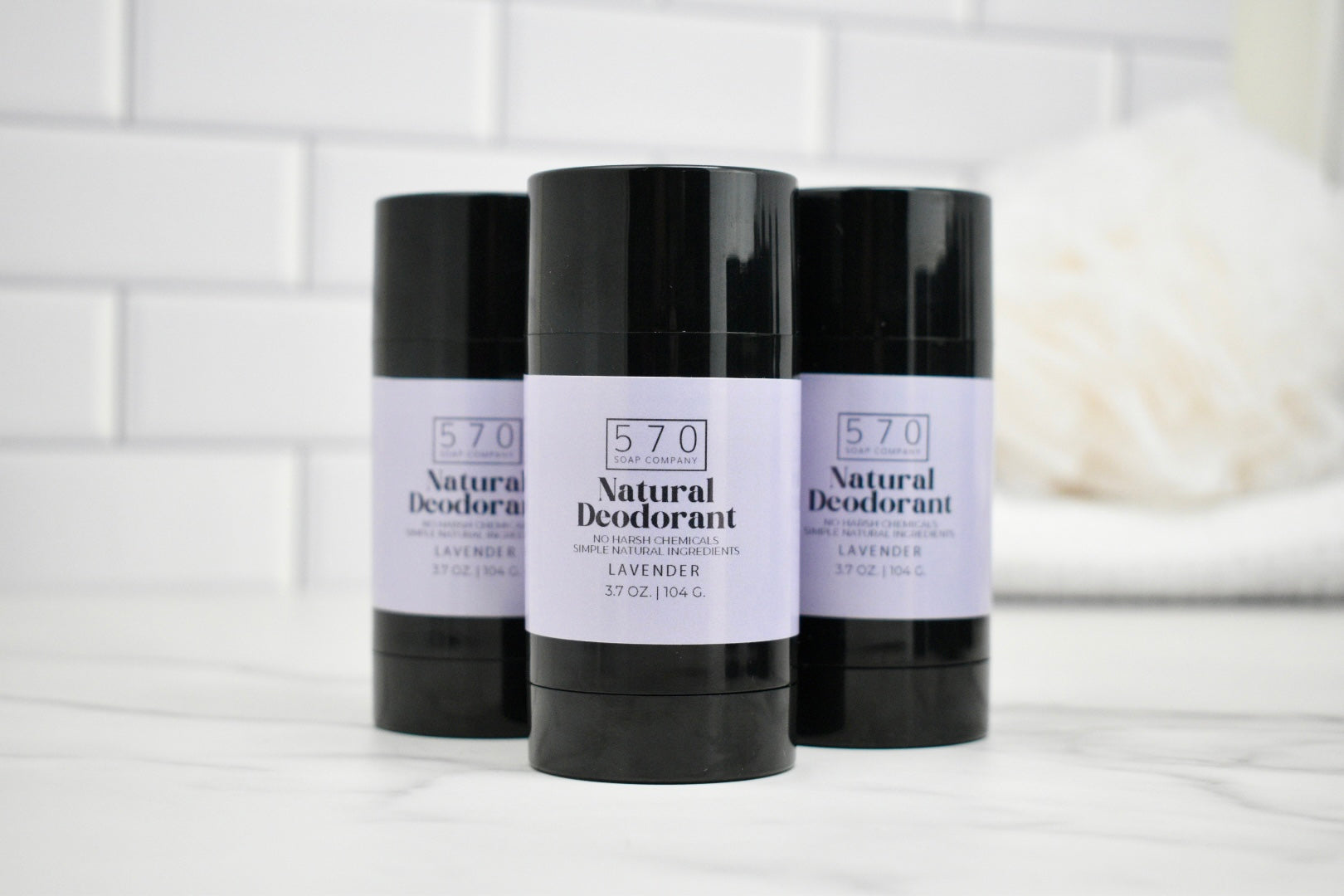Three bottles of 570 Natural Deodorant on a white surface with a tiled wall background.