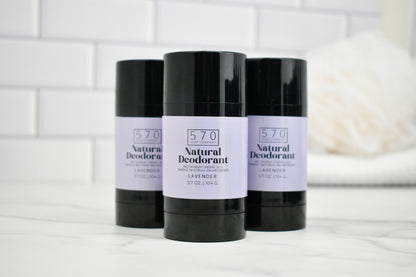 Three bottles of 570 Natural Deodorant on a white surface with a tiled wall background.