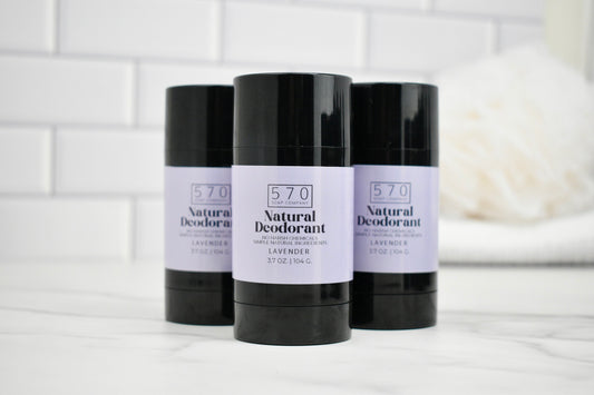 Three bottles of 570 Natural Deodorant on a white surface with a tiled wall background.