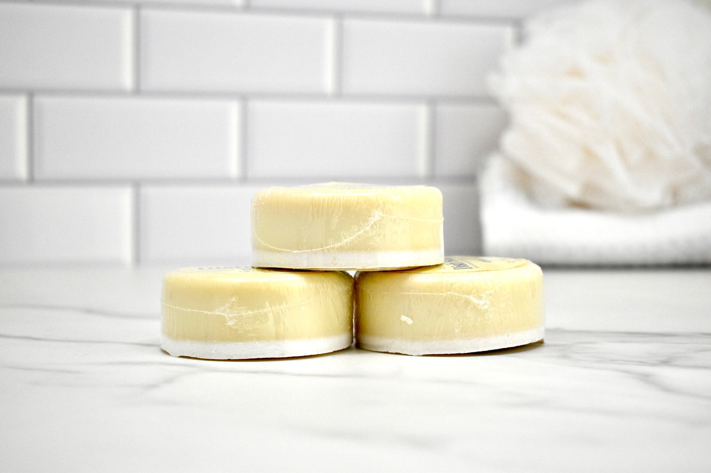 Three bars of soap stacked on a white surface with a tiled wall background