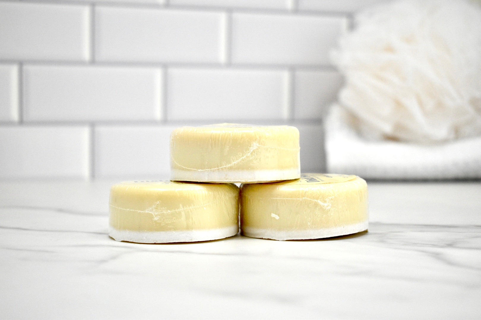 Three bars of soap stacked on a white surface with a tiled wall background