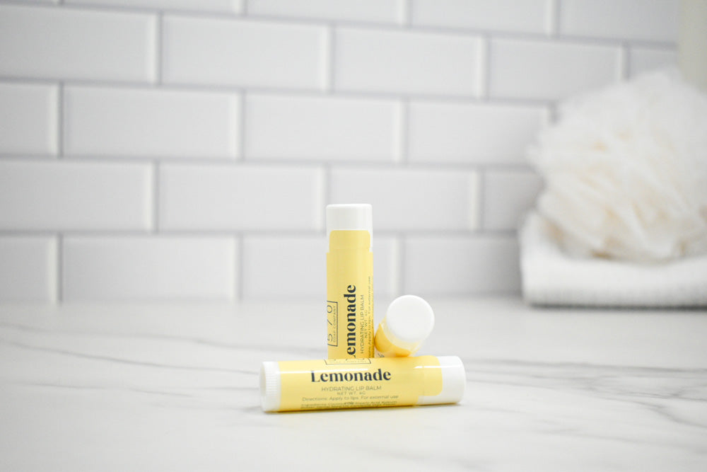 Two lip balm tubes labeled 'Lemonade' on a bathroom counter with a tiled wall background.