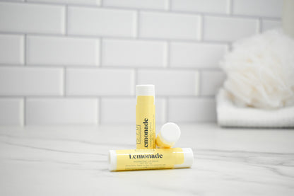Two lip balm tubes labeled 'Lemonade' on a bathroom counter with a tiled wall background.