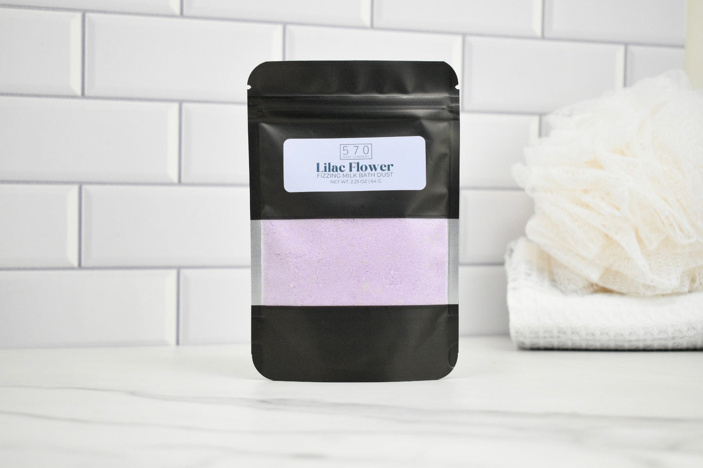 Black packaging of lilac flower product on a white tiled background