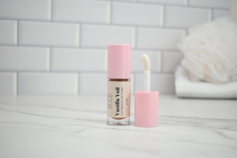 Vanilla Vell lip gloss with applicator on a white surface against a tiled wall background