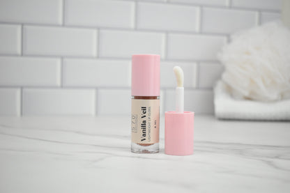 Vanilla Vell lip gloss with applicator on a white surface against a tiled wall background