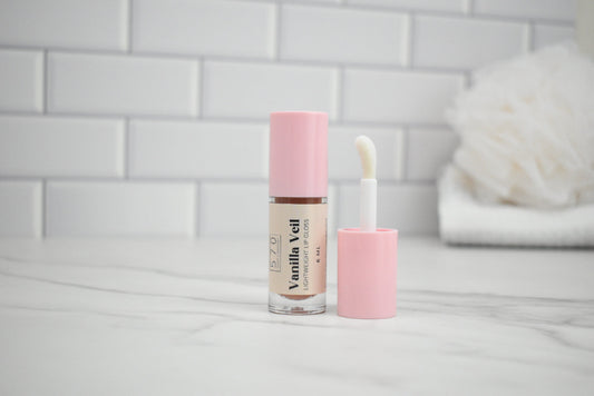 Vanilla Vell lip gloss with applicator on a white surface against a tiled wall background