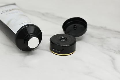 A black tube of 570 Soap Co.'s Lightweight Lotion, with an open cap, rests on a white marble surface. The tube's end is silver, and the cap features a gold accent near its hinge, adding an elegant touch.