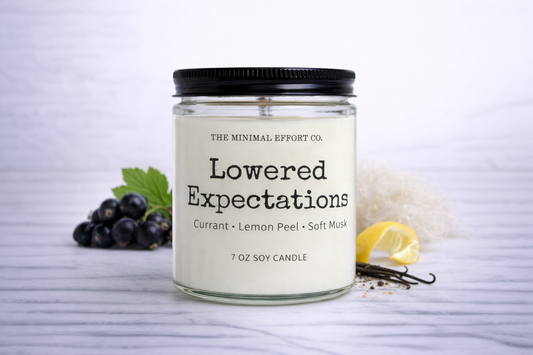 Candle labeled 'Lowered Expectations' from The Minimal Effort Co. with ingredients listed on a white background.