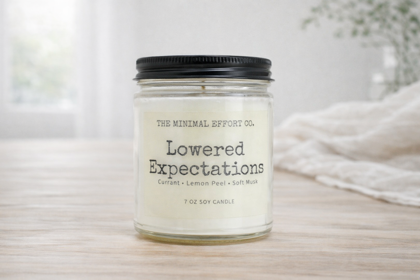 Candle jar labeled 'Lowered Expectations' by The Minimal Effort Co. on a neutral background.
