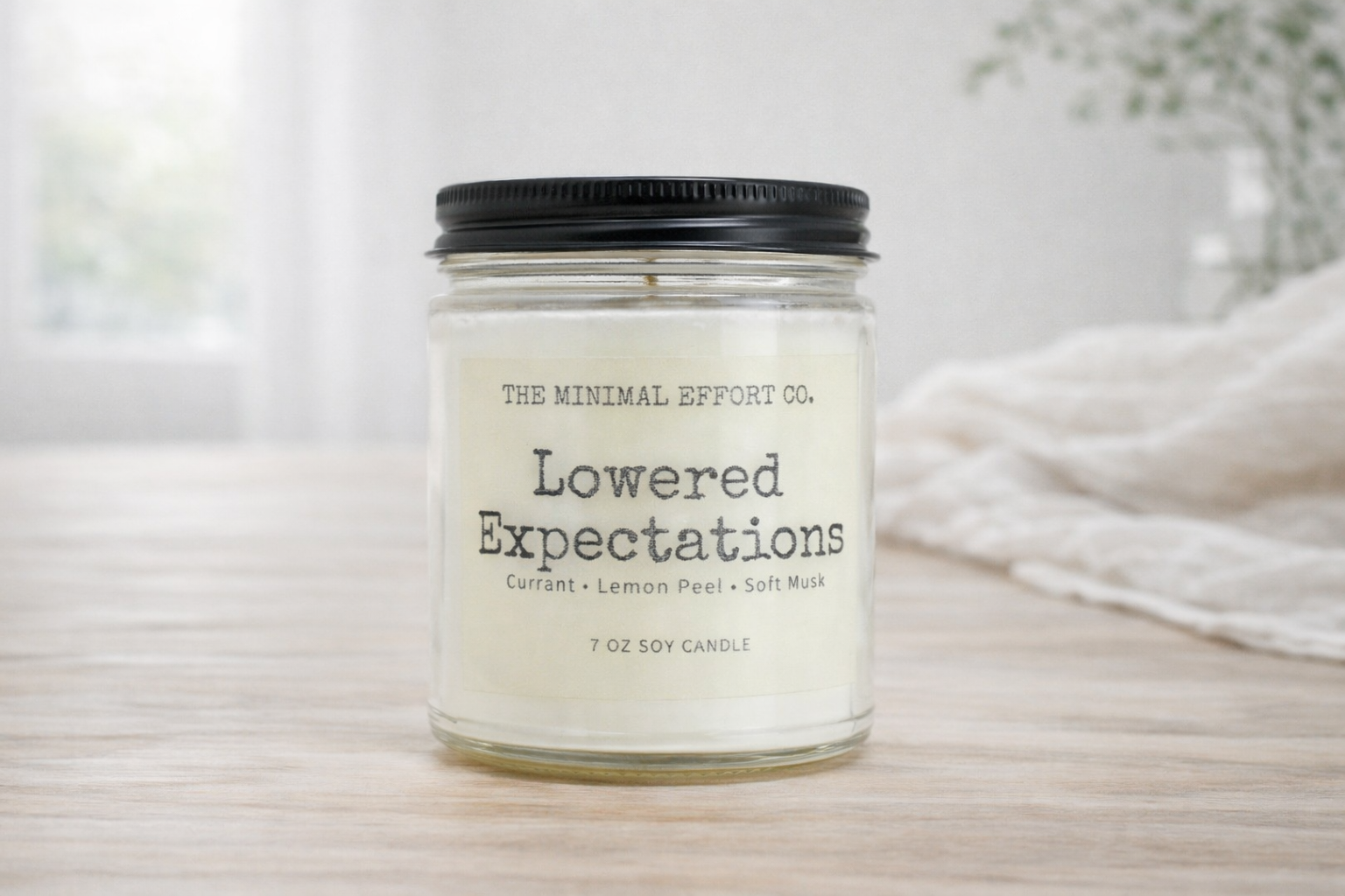 Candle jar labeled 'Lowered Expectations' by The Minimal Effort Co. on a neutral background.