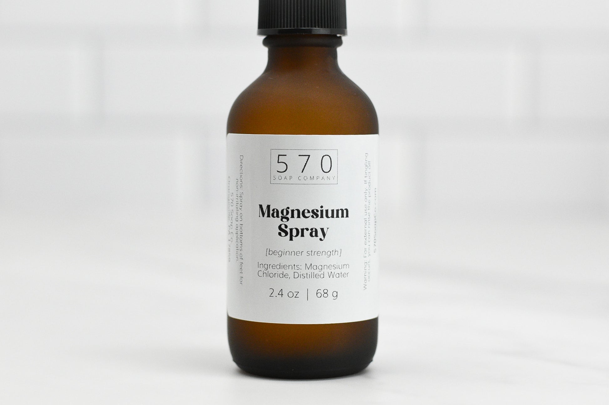 A brown bottle with a black cap labeled 570 Soap Co. Magnesium Spray (beginner strength). It contains magnesium chloride and distilled water, holding 2.4 oz or 68 g, placed on a white surface.