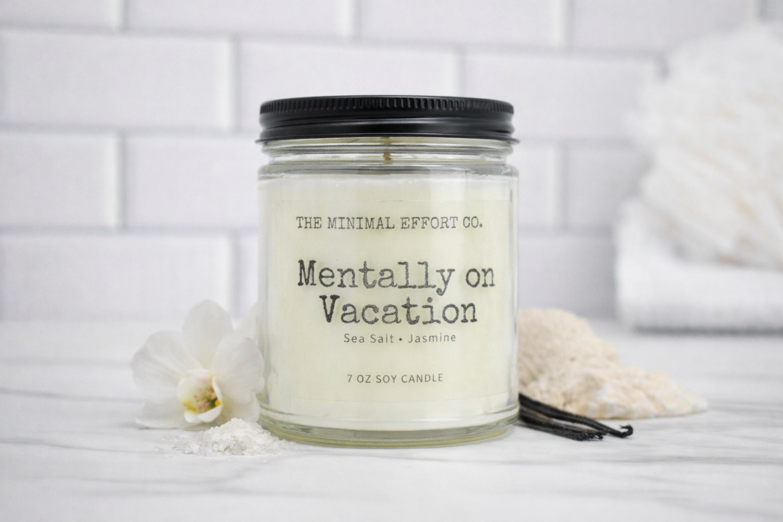 Candle jar labeled 'Mentally on Vacation' by The Minimal Effort Co. on a white surface with decorative elements.