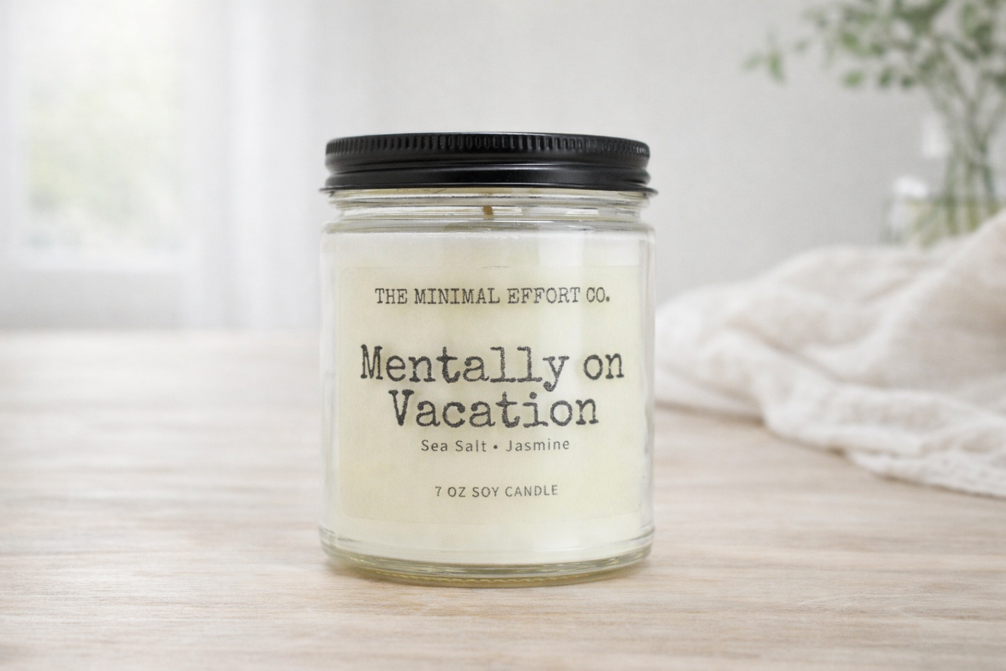 Candle jar labeled 'Mentally on Vacation' by The Minimal Effort Co. on a light surface.