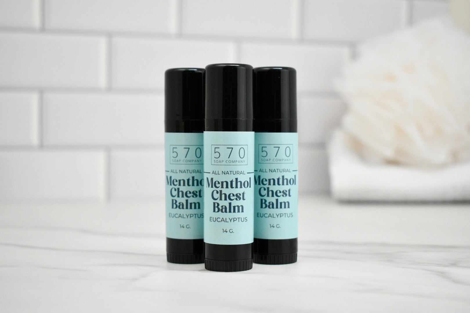 Three sticks of 570 Menthol Chest Balm on a white surface with a tiled wall background.