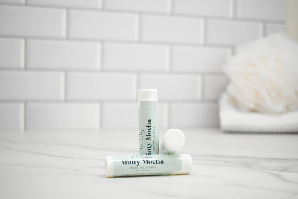 Two lip balm tubes labeled 'Minty Mocha' on a bathroom counter with a tiled wall background.