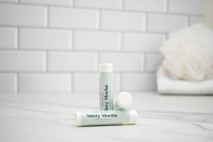 Two lip balm tubes labeled 'Minty Mocha' on a bathroom counter with a tiled wall background.