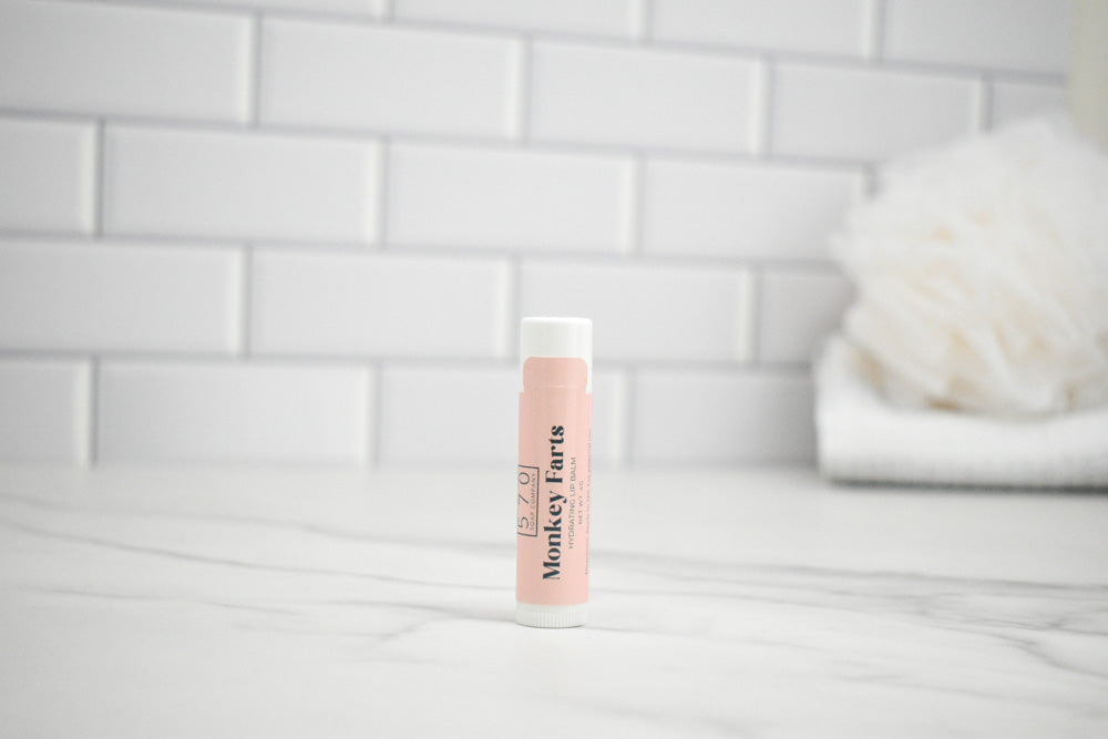 Lip balm with 'Monkey Farts' branding on a white surface with a tiled wall background