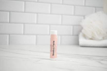 Lip balm with 'Monkey Farts' branding on a white surface with a tiled wall background