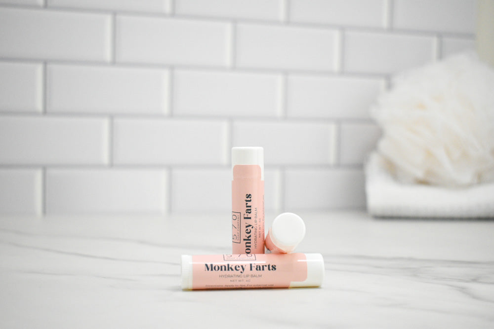 Two lip balms labeled 'Monkey Farts' on a white surface with a tiled wall background.