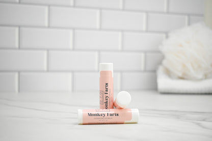 Two lip balms labeled 'Monkey Farts' on a white surface with a tiled wall background.
