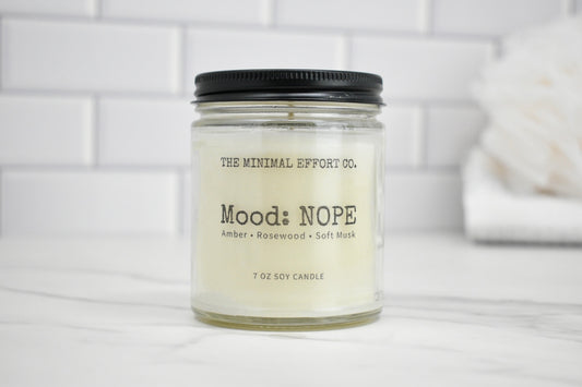 Candle jar labeled 'Mood: NOPE' by The Minimal Effort Co. on a white surface with a tiled wall background.