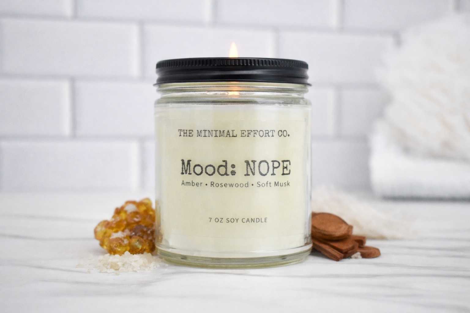 Candle in a glass jar with a black lid on a white surface, featuring 'The Minimal Effort Co.' branding.