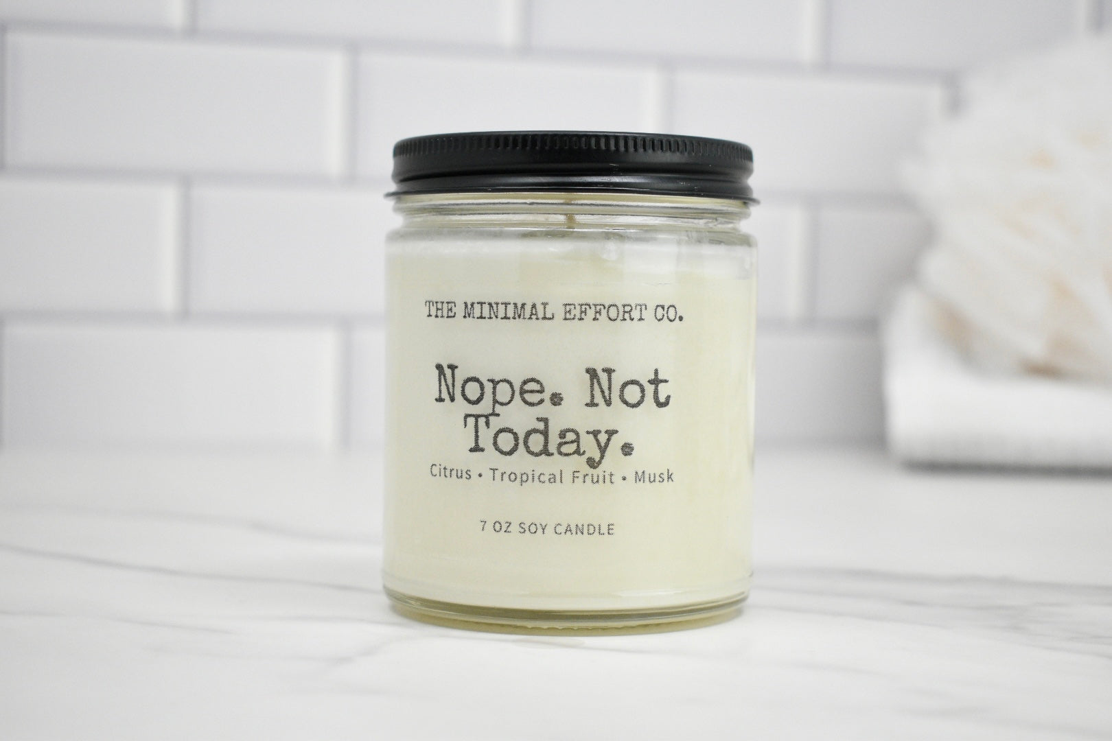 Candle jar labeled 'Nope. Not Today.' by The Minimal Effort Co. on a white surface with a tiled wall background.