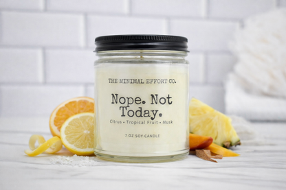 Candle jar labeled 'Nope. Not Today.' from The Minimal Effort Co. with lemons and citrus peels on a white surface.