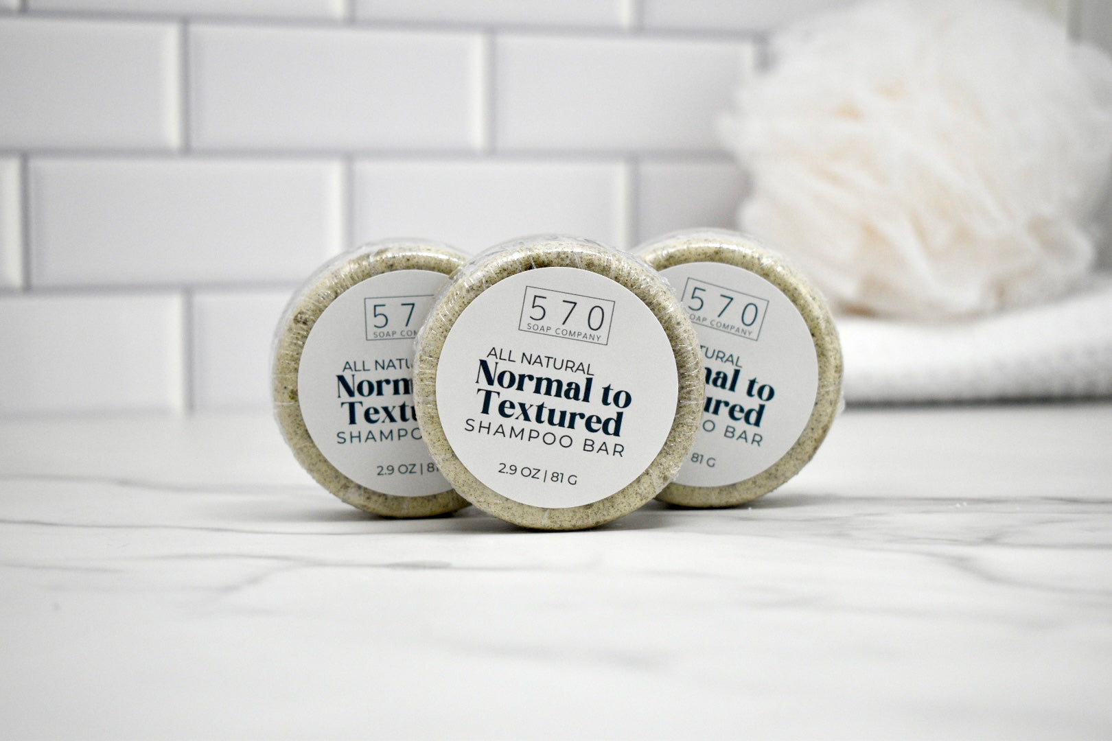 Three shampoo bars labeled '570' on a white surface with a tiled wall background.