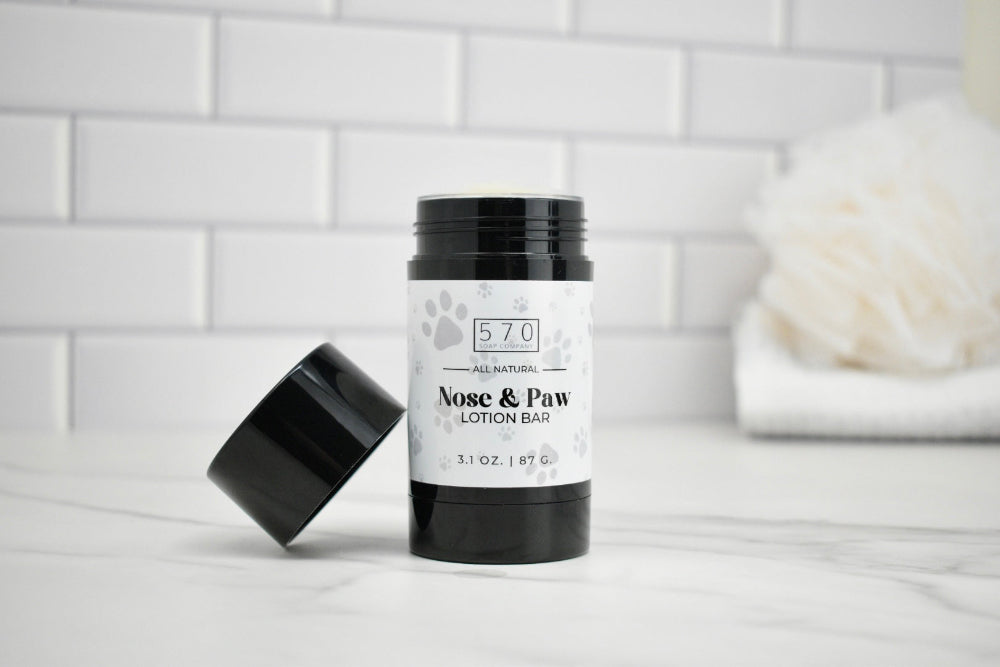 Nose and paw lotion bar with black lid on a white surface against a tiled wall background