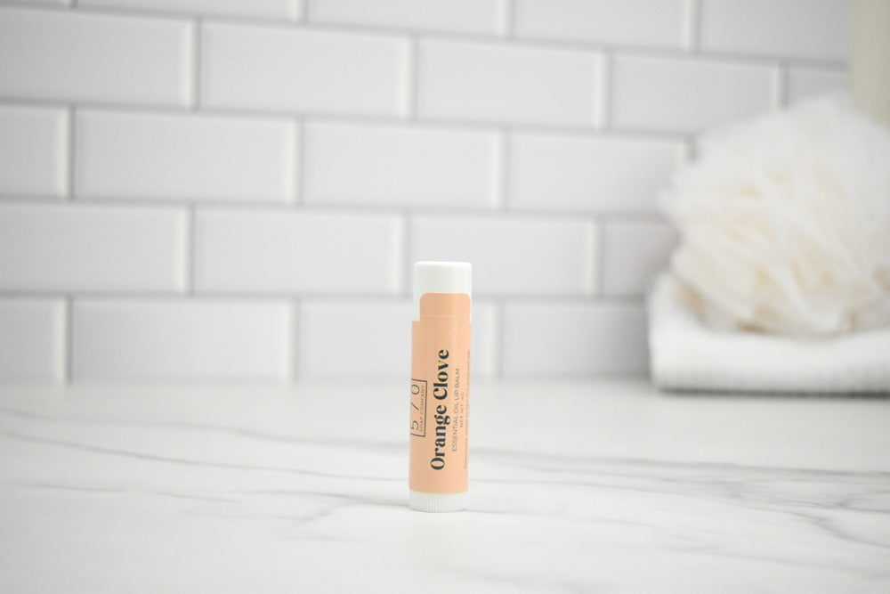 Lip balm with 'Orange Clove' flavor on a white surface with a tiled wall background