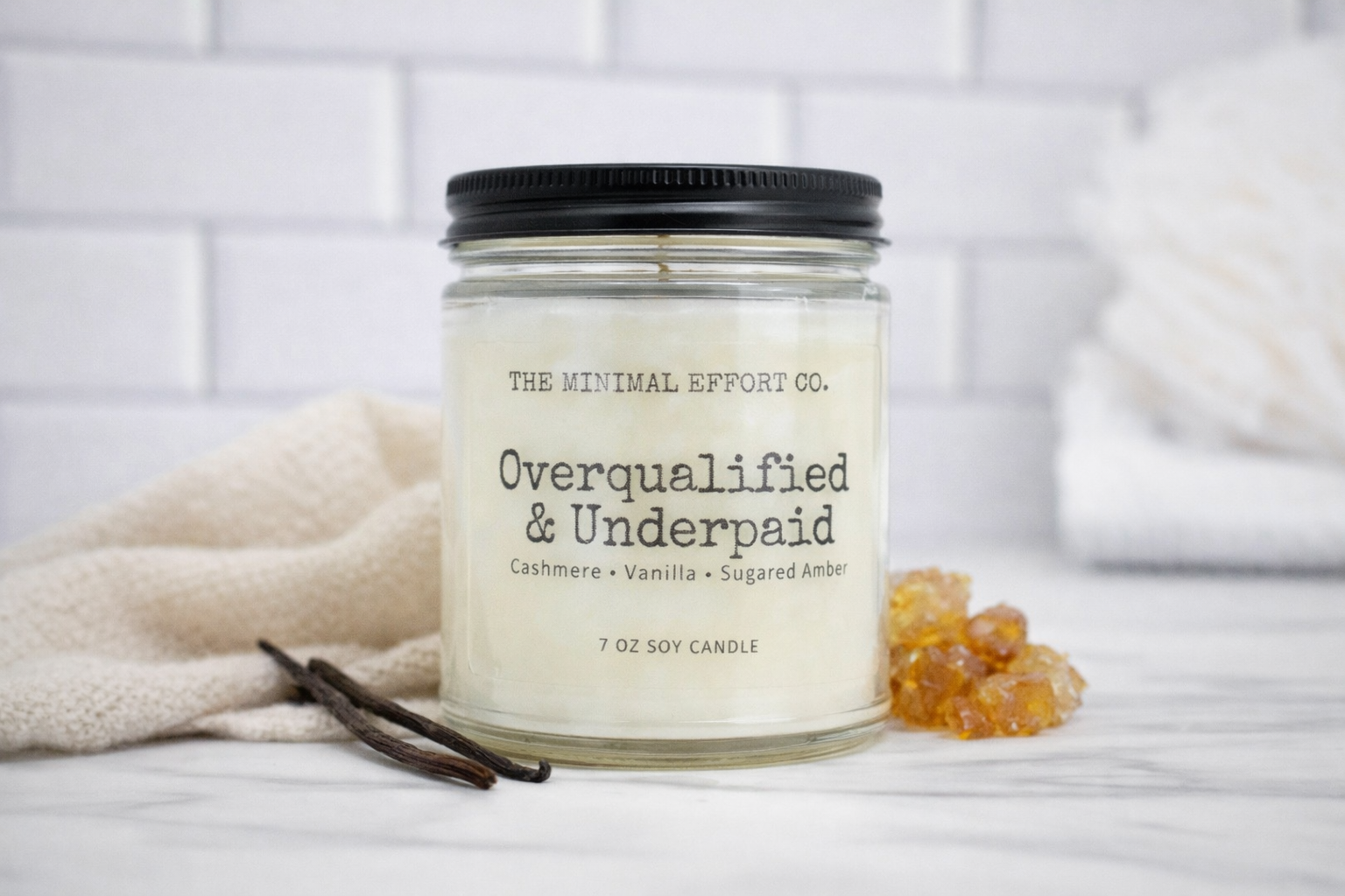 Candle jar with 'The Minimal Effort Co.' label on a white surface with vanilla beans and amber gummy bears.