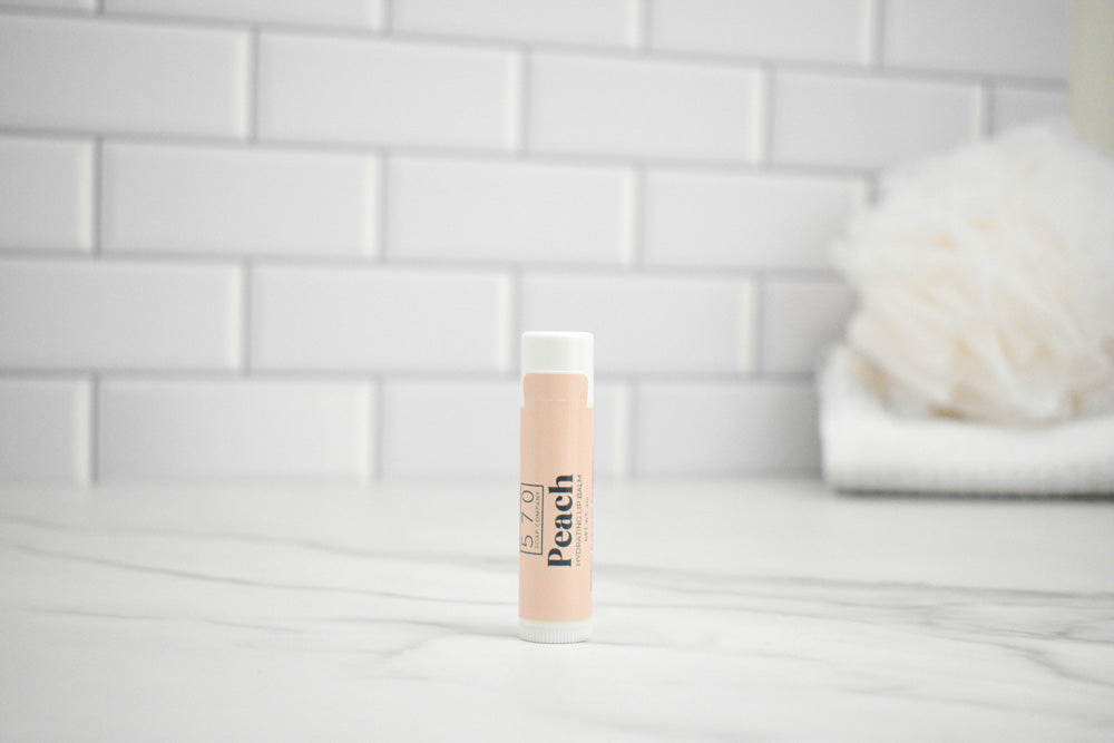 Lip balm labeled 'Peach' on a bathroom counter with a tiled wall background
