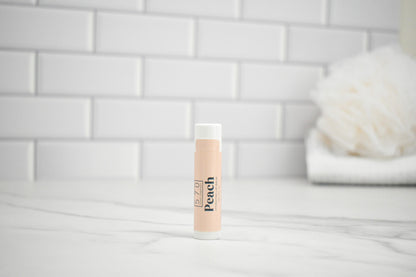Lip balm labeled 'Peach' on a bathroom counter with a tiled wall background