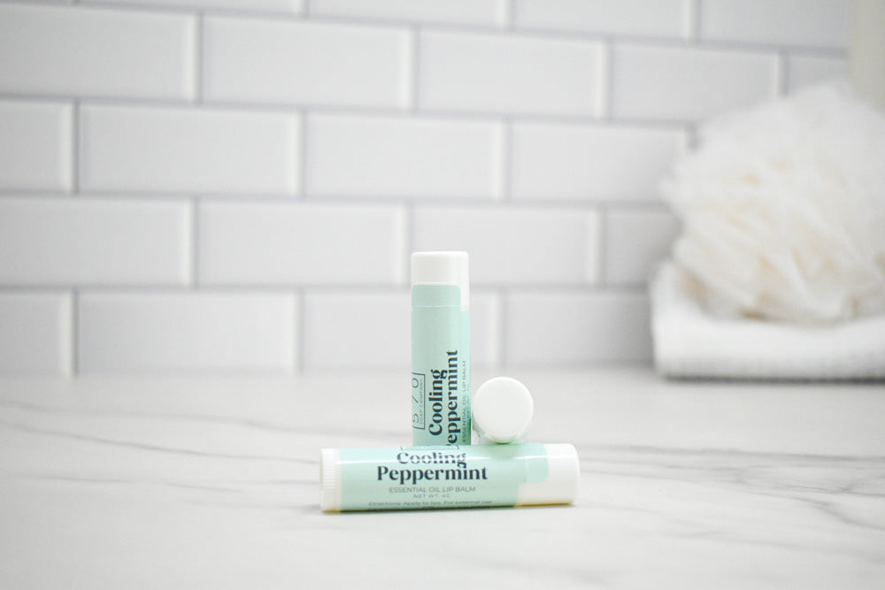 Two lip balm tubes labeled 'Cooling Peppermint' on a bathroom counter with a tiled wall background.