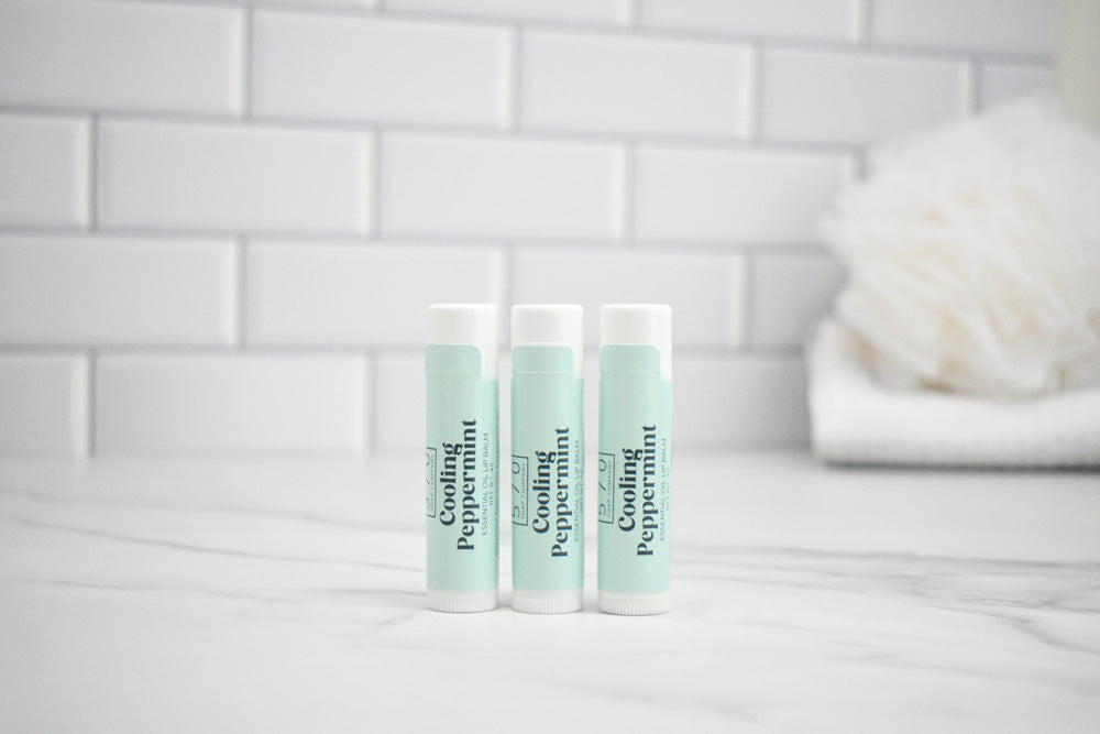 Two lip balm tubes labeled 'Cooling Peppermint' on a white surface with a tiled wall background.