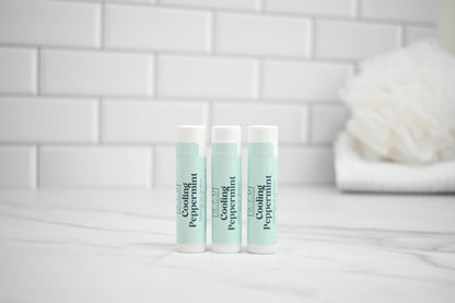 Two lip balm tubes labeled 'Cooling Peppermint' on a white surface with a tiled wall background.
