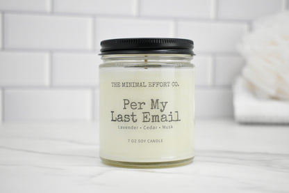 Candle jar labeled 'Per My Last Email' by The Minimal Effort Co. on a white surface with a tiled wall background.