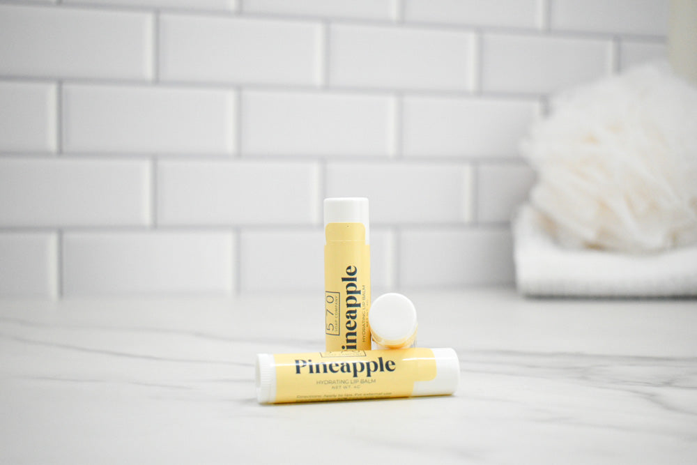 Two lip balm tubes labeled 'Pineapple' on a bathroom counter with a tiled wall background.