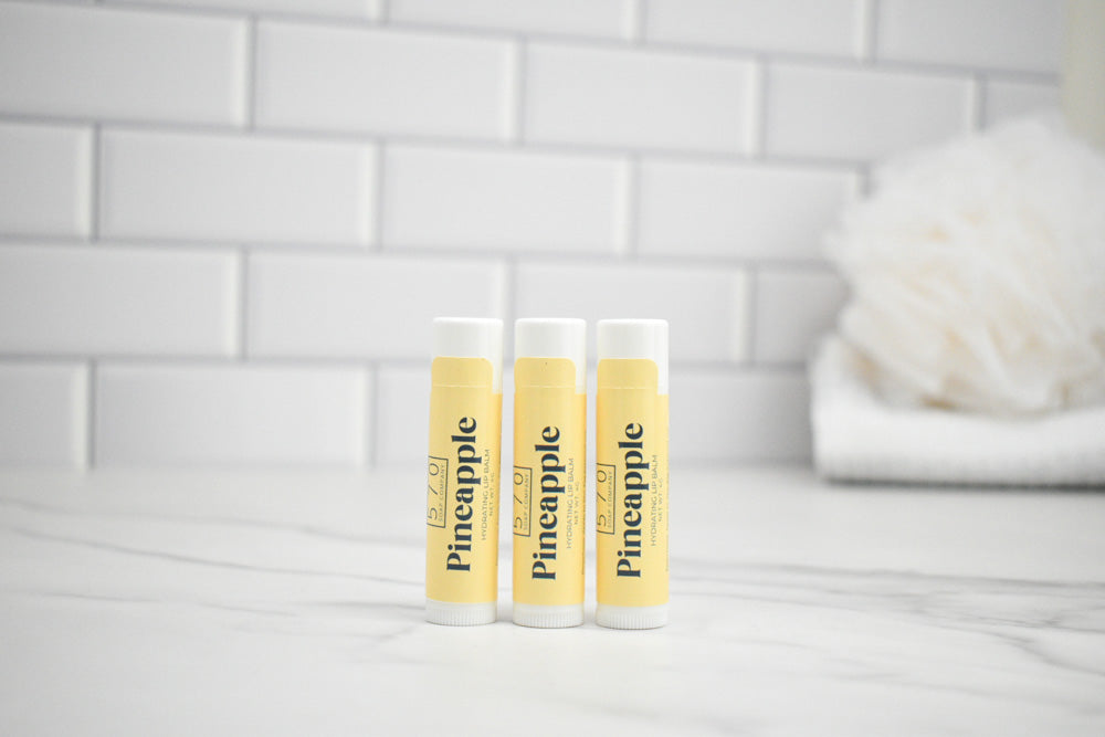 Three lip balm tubes with pineapple flavor on a white surface and tiled wall background