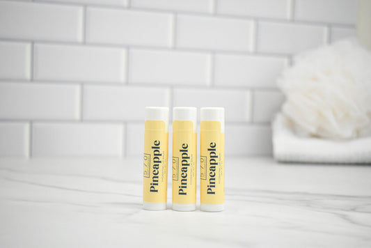 Three lip balm tubes with pineapple flavor on a white surface and tiled wall background
