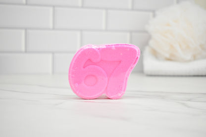 Pink bath bomb with the number 67 on a white surface