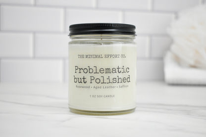 Candle jar labeled 'Problematic but Polished' by The Minimal Effort Co. on a white surface with a tiled wall background.